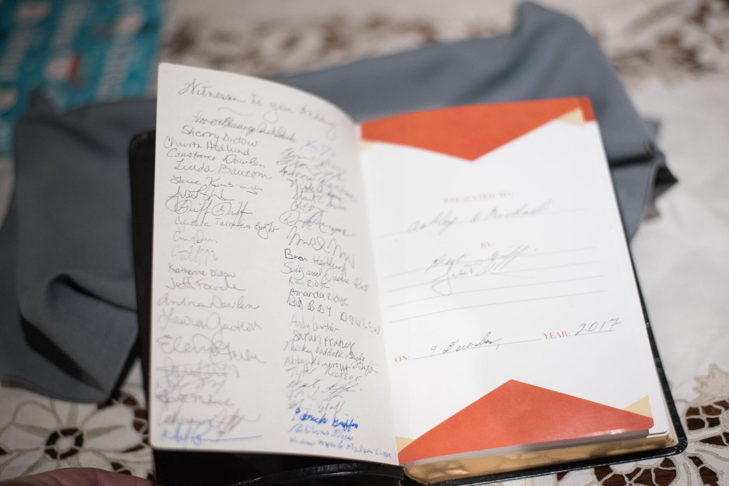 Open guest book with signatures on left page and orange geometric design on right page, resting on a table.