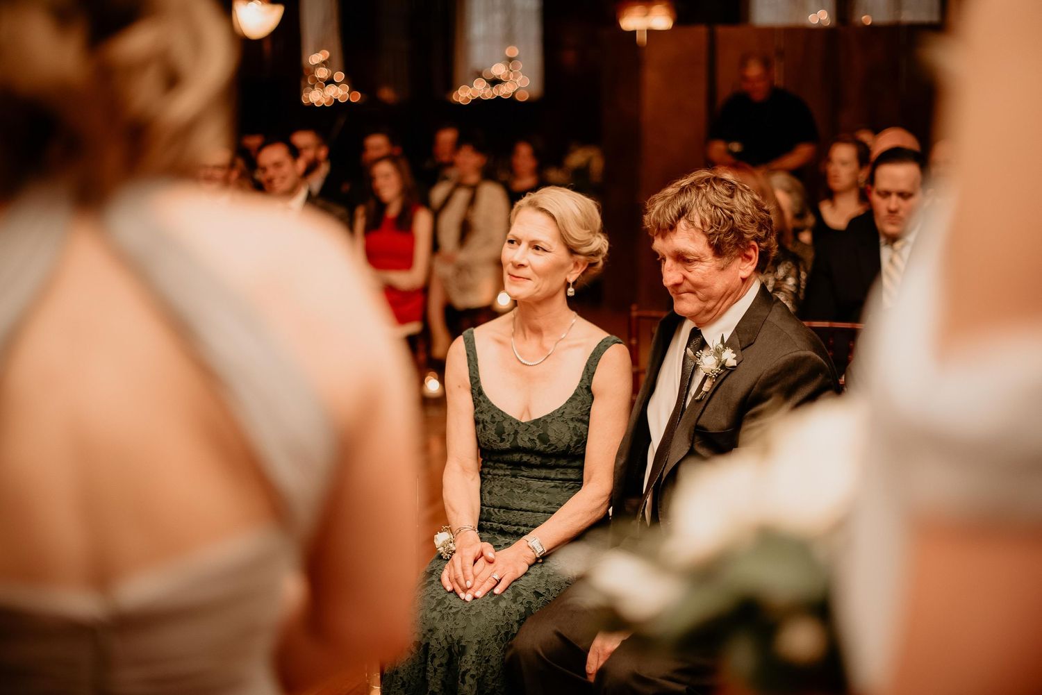 Smiling wedding guests seated in pews watching the bride during a wedding ceremony.