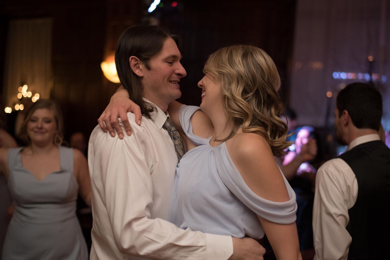 A couple shares a joyful dance at a wedding reception, smiling warmly at each other in elegant attire.