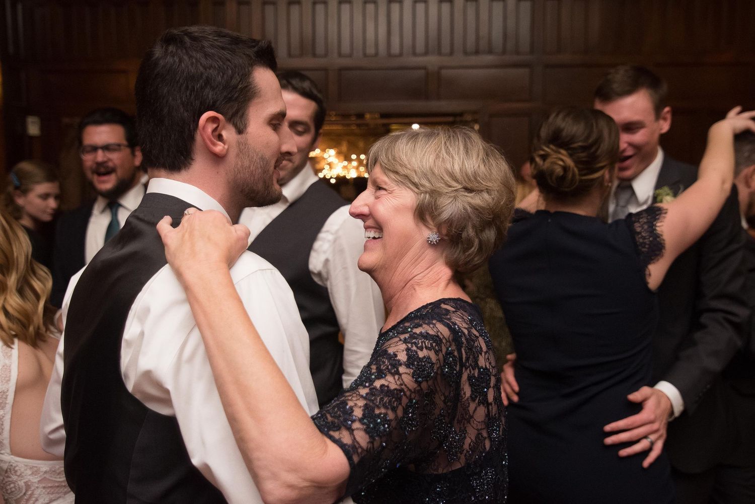 Mother and son share a joyful dance at a wedding reception, surrounded by guests celebrating.
