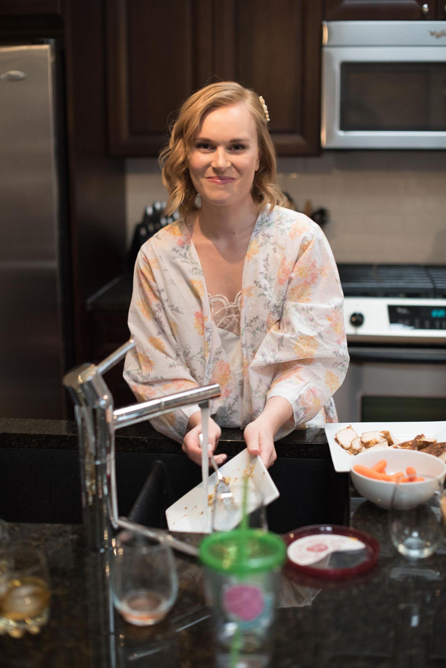 Woman in floral robe smiling while preparing food at a kitchen counter with granite countertops.