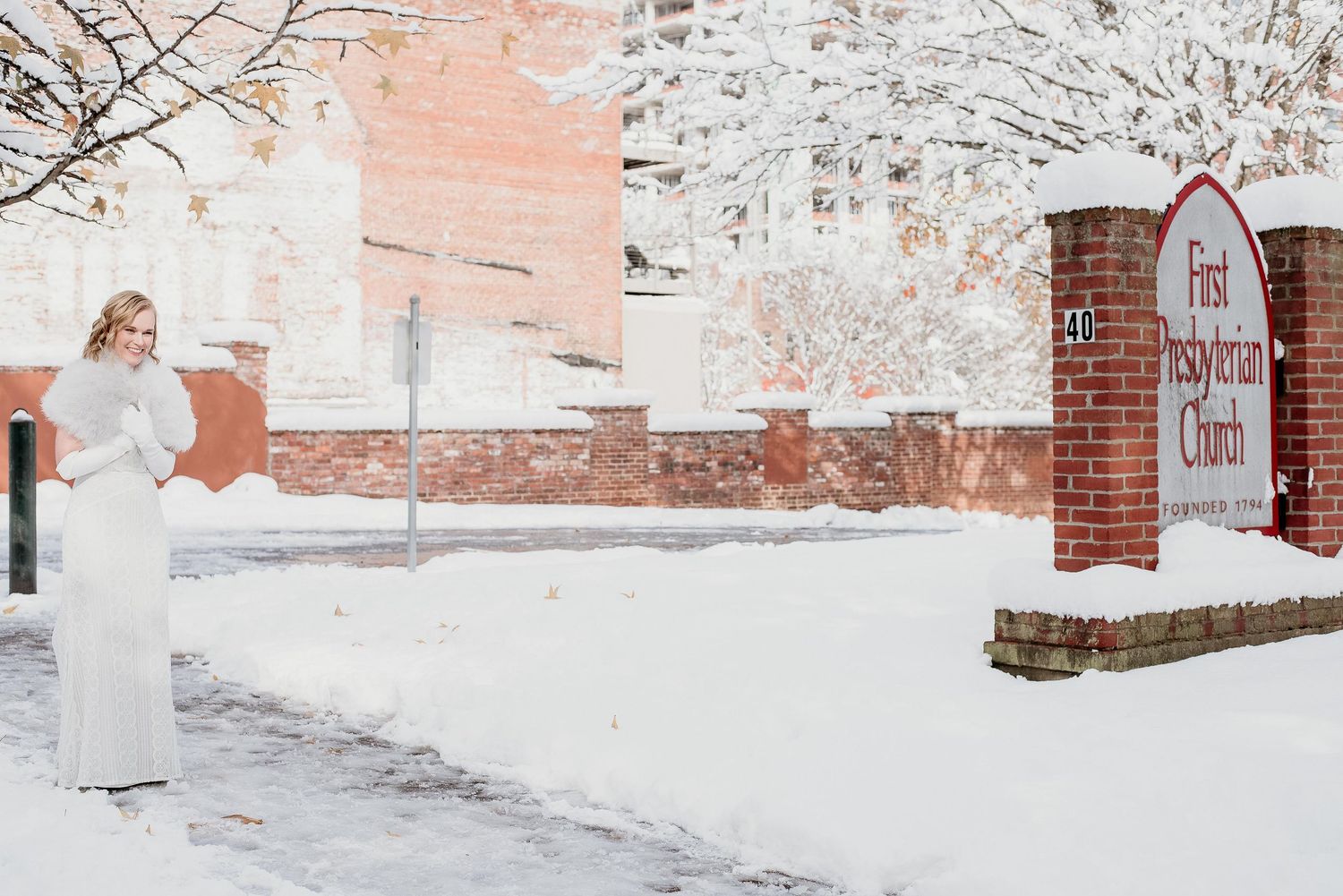 Pregnant woman in white dress poses in snow outside First Presbyterian Church in winter.