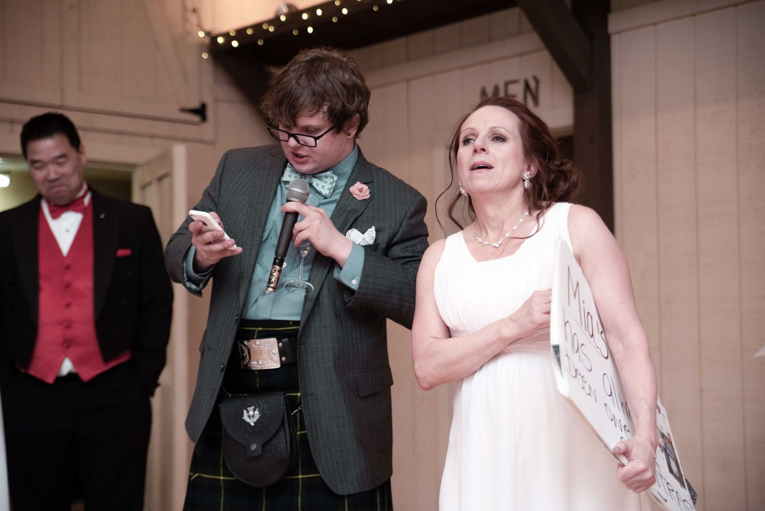 Wedding guests in formal attire, including a kilt, celebrate at an indoor reception venue.