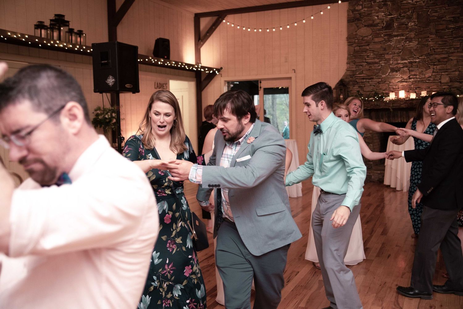 Guests dancing joyfully at a rustic wedding reception in a warmly lit barn venue.