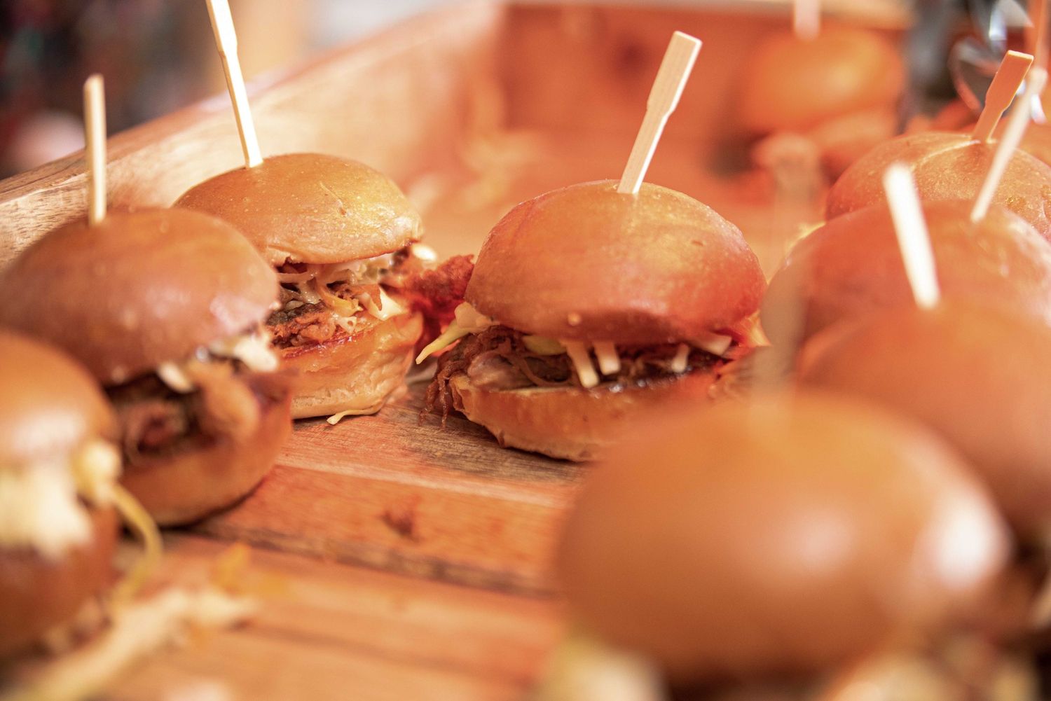 Mini pulled pork sliders on brioche buns served on a rustic wooden board, garnished with toothpicks.