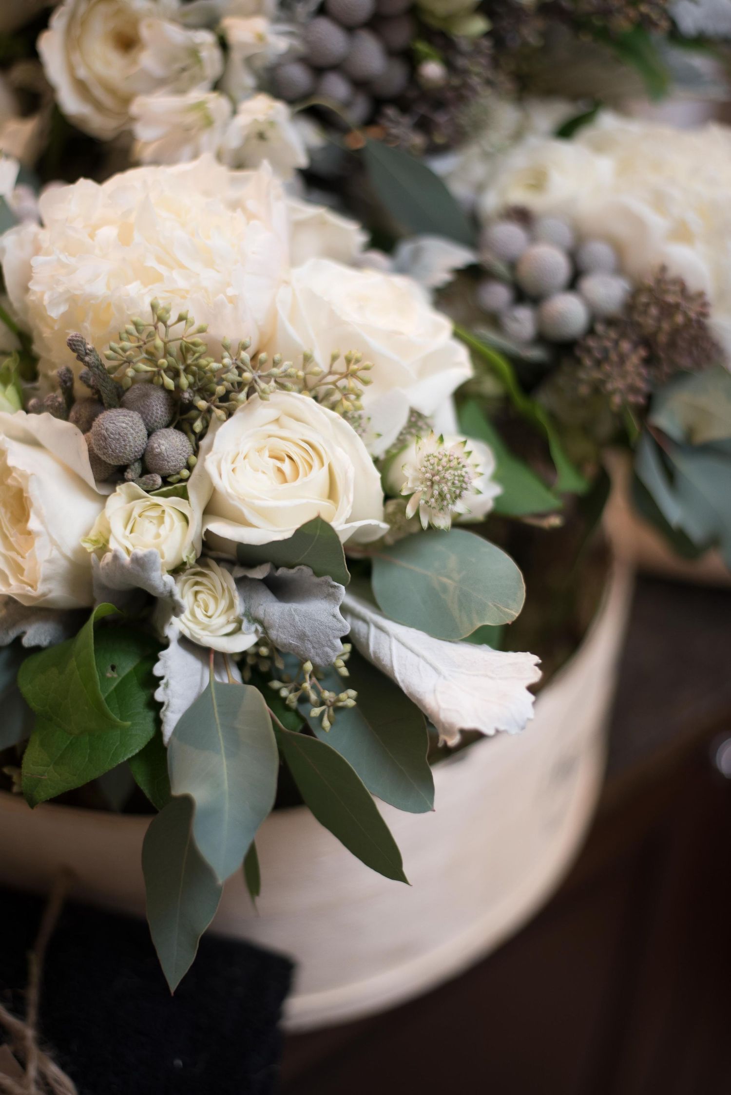 Elegant white roses and eucalyptus bouquet with silver brunia berries in a rustic wooden container.