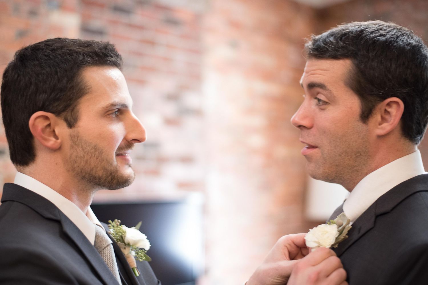 Two grooms in suits adjusting boutonnieres at their wedding ceremony.