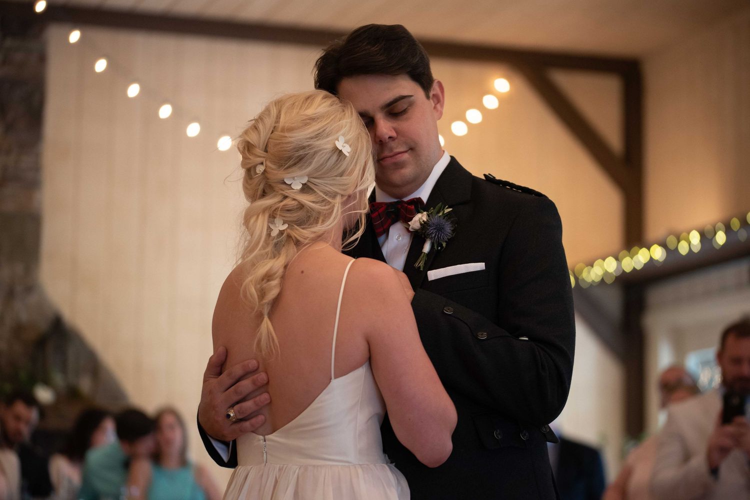 Bride and groom share their first dance at a rustic barn wedding venue with warm string lights.