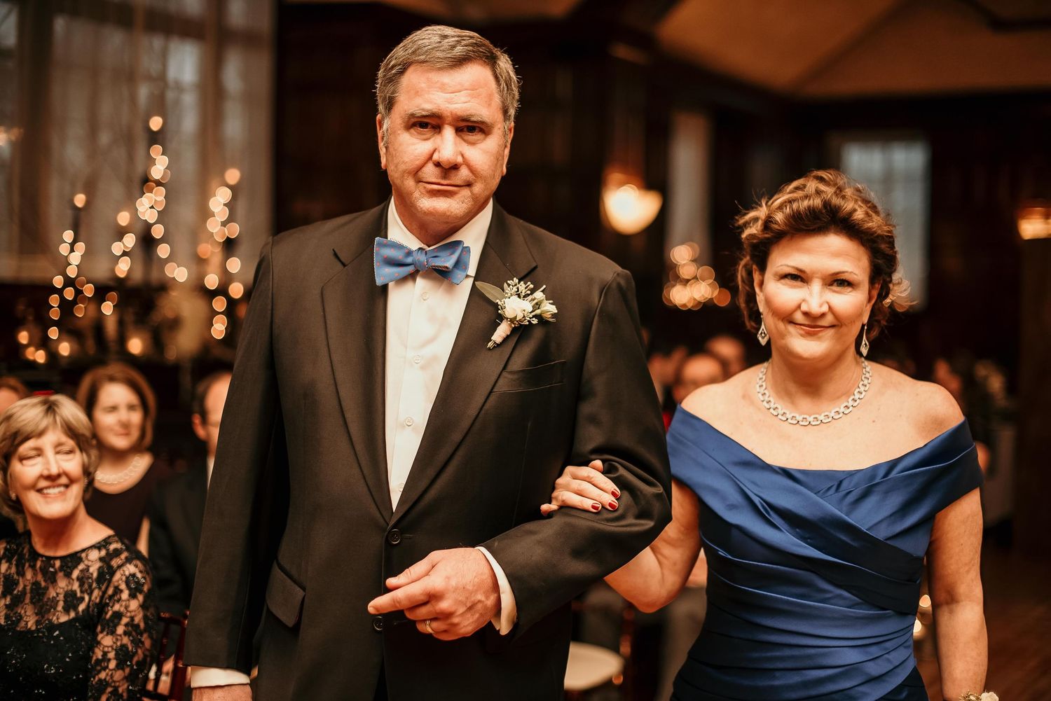 Elegant couple in formal attire walking at a wedding reception, man in tuxedo and woman in blue gown.