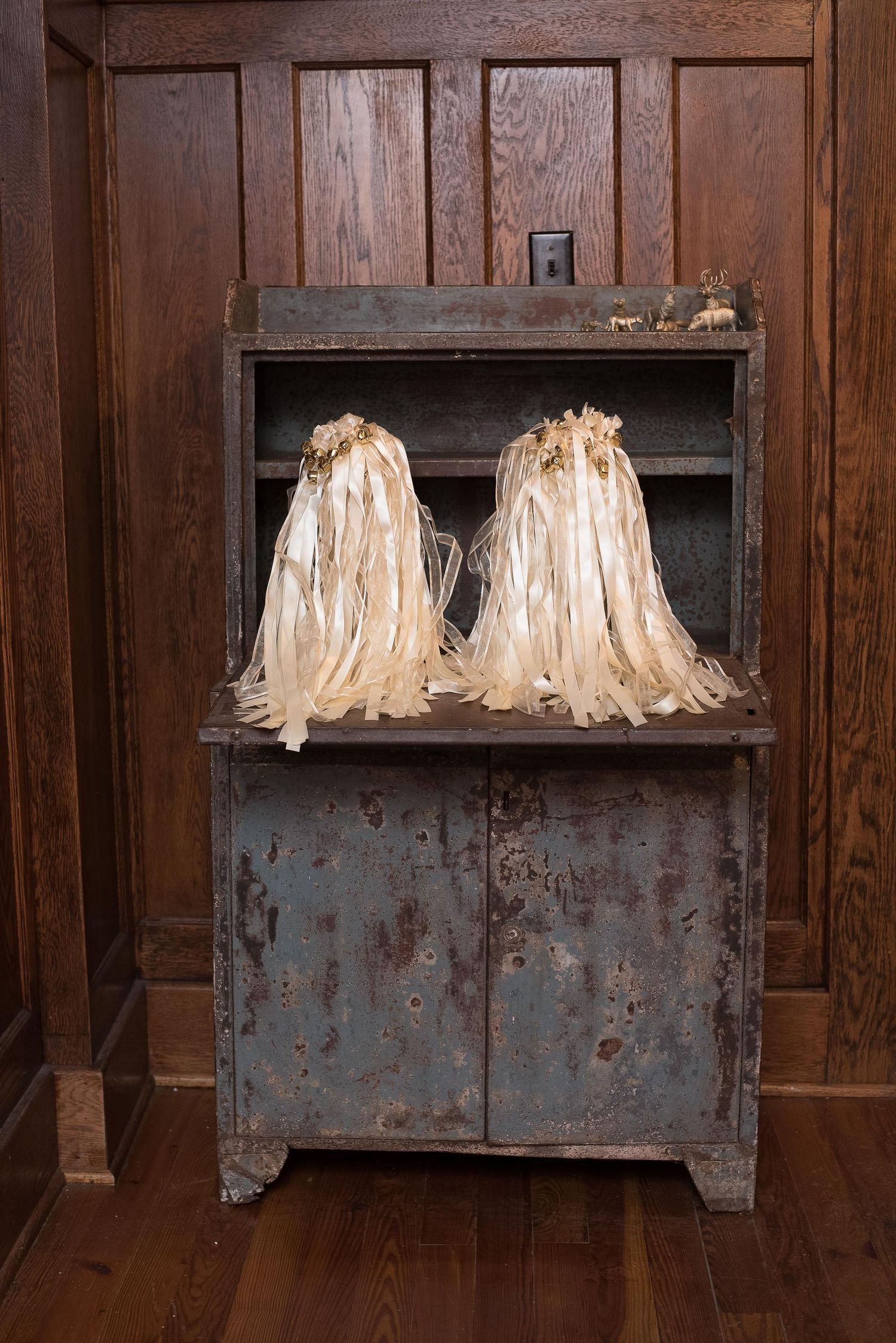 Two cream ribbon decorations on a rustic blue metal cabinet against dark wood paneling.
