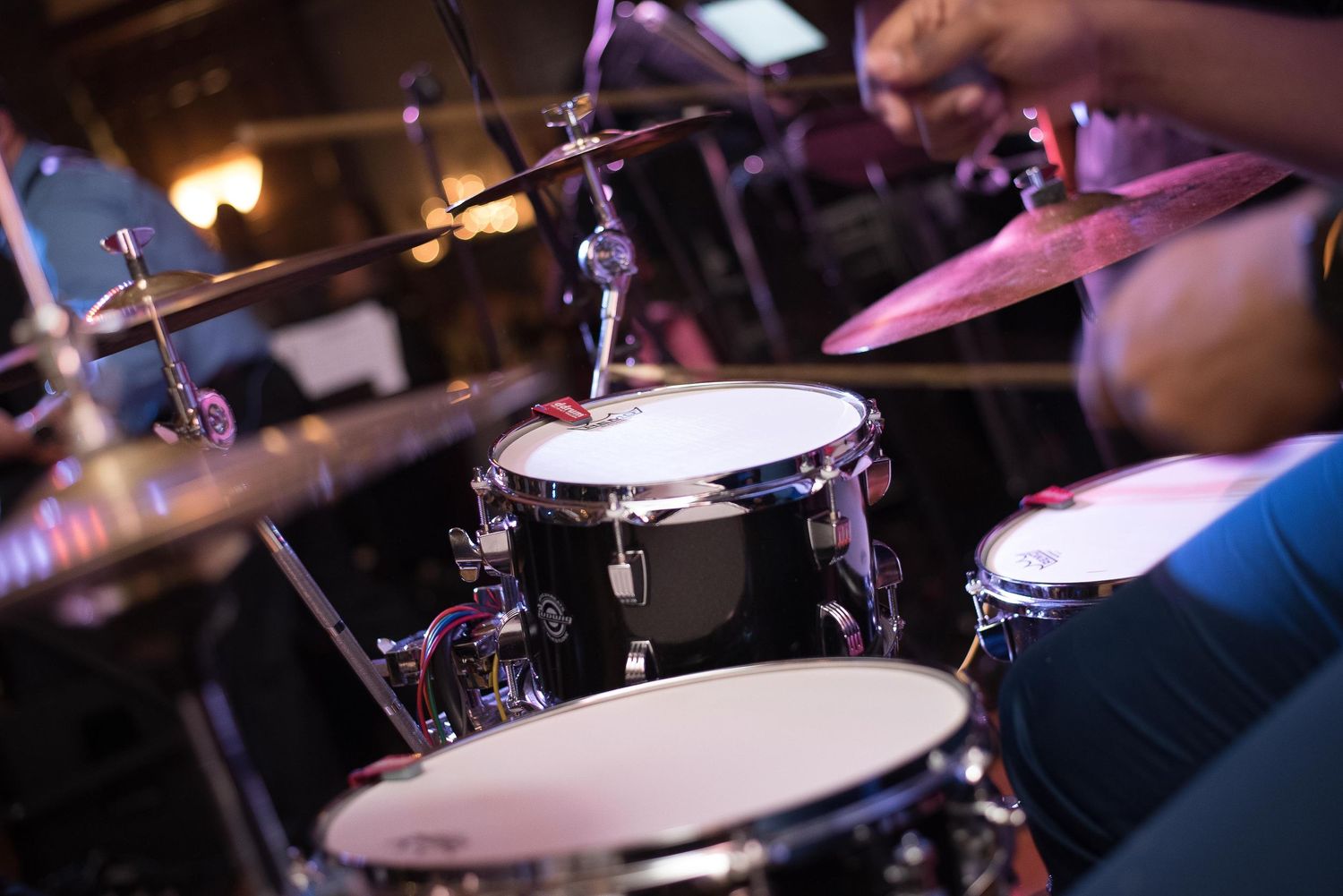 Close-up of a drummer performing on a black drum kit with cymbals at a live music event.