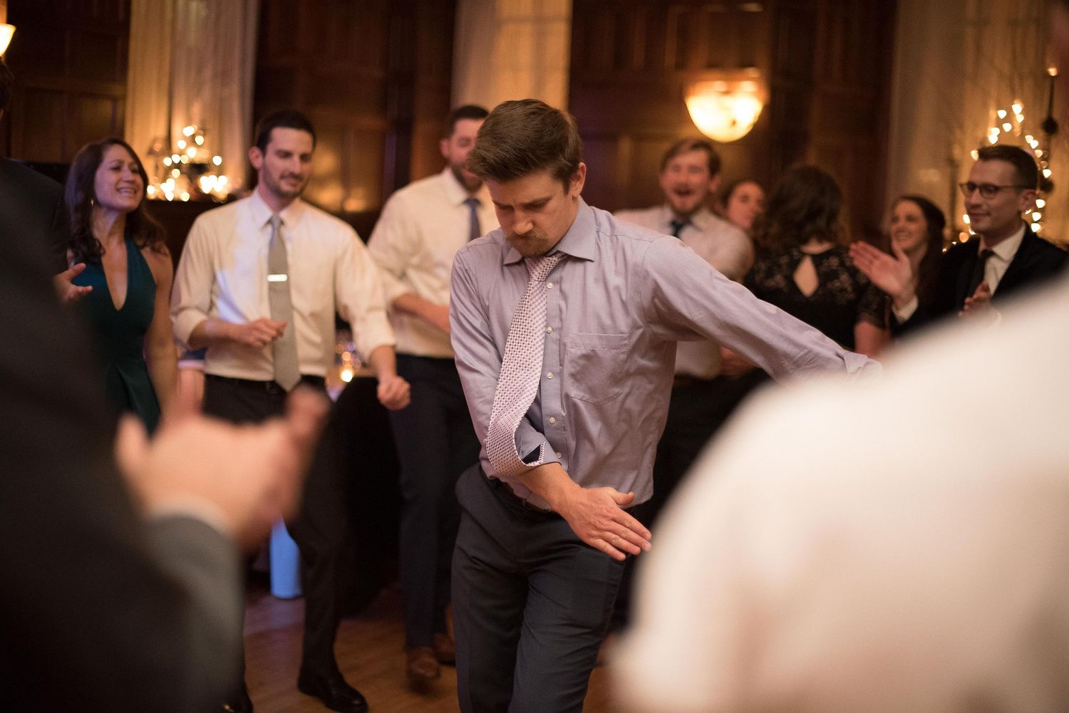Man dancing energetically at a wedding reception in an elegant ballroom with guests celebrating in the background.
