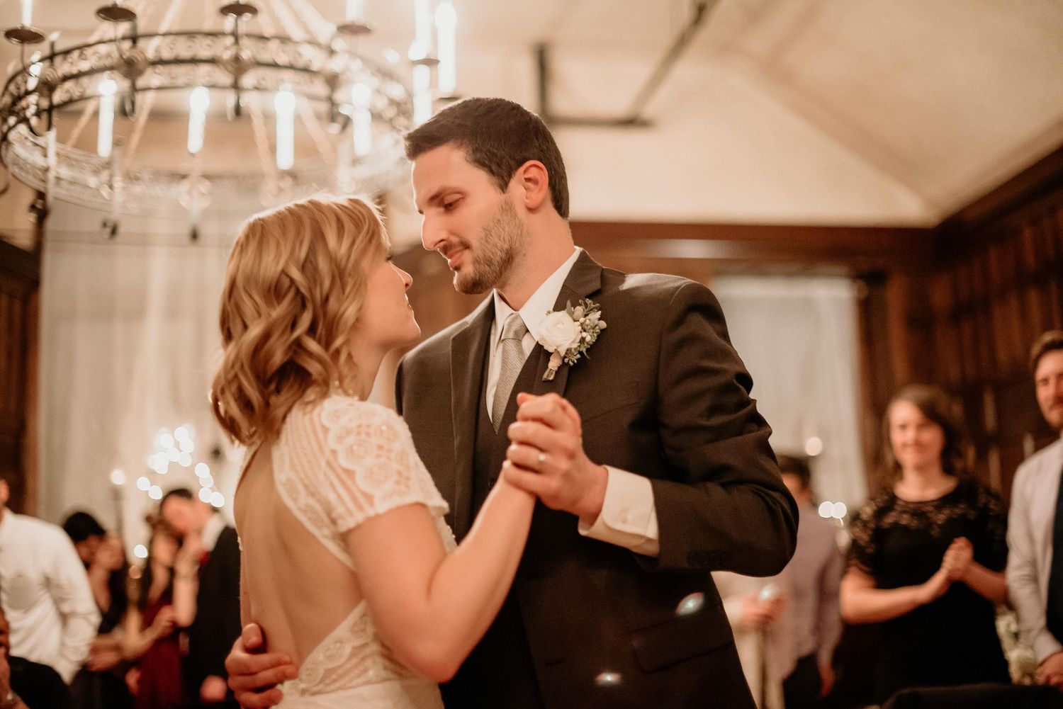 A bride and groom share their first dance under a chandelier at an elegant wedding reception.