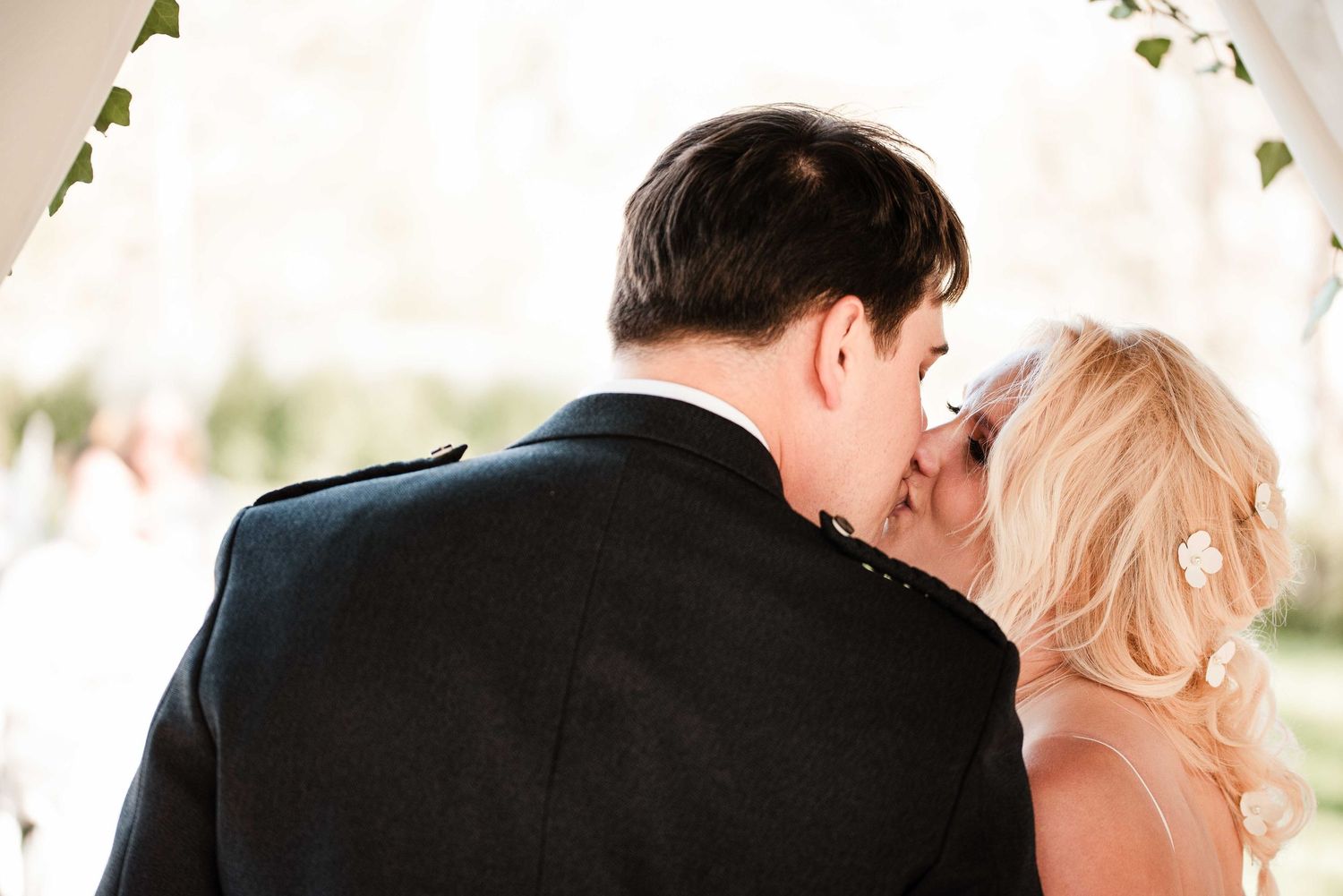 Bride and groom sharing their first kiss at the wedding altar, surrounded by lush greenery.