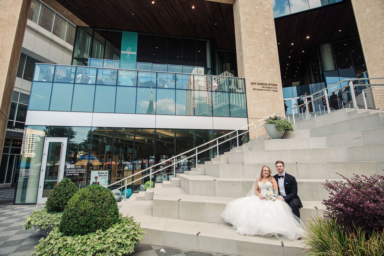 Bride and groom sitting on steps outside modern glass building after ceremony.