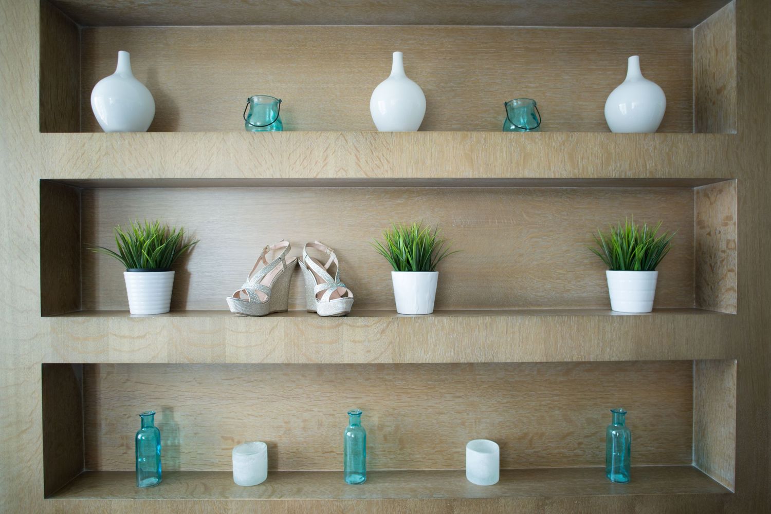 Wooden shelves styled with white vases, bridal heels, green plants, and teal glass bottles.