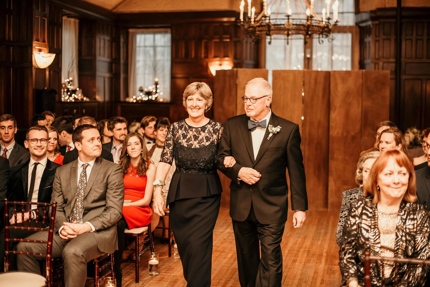 Elegant couple walking down the aisle at a formal indoor wedding ceremony with seated guests.