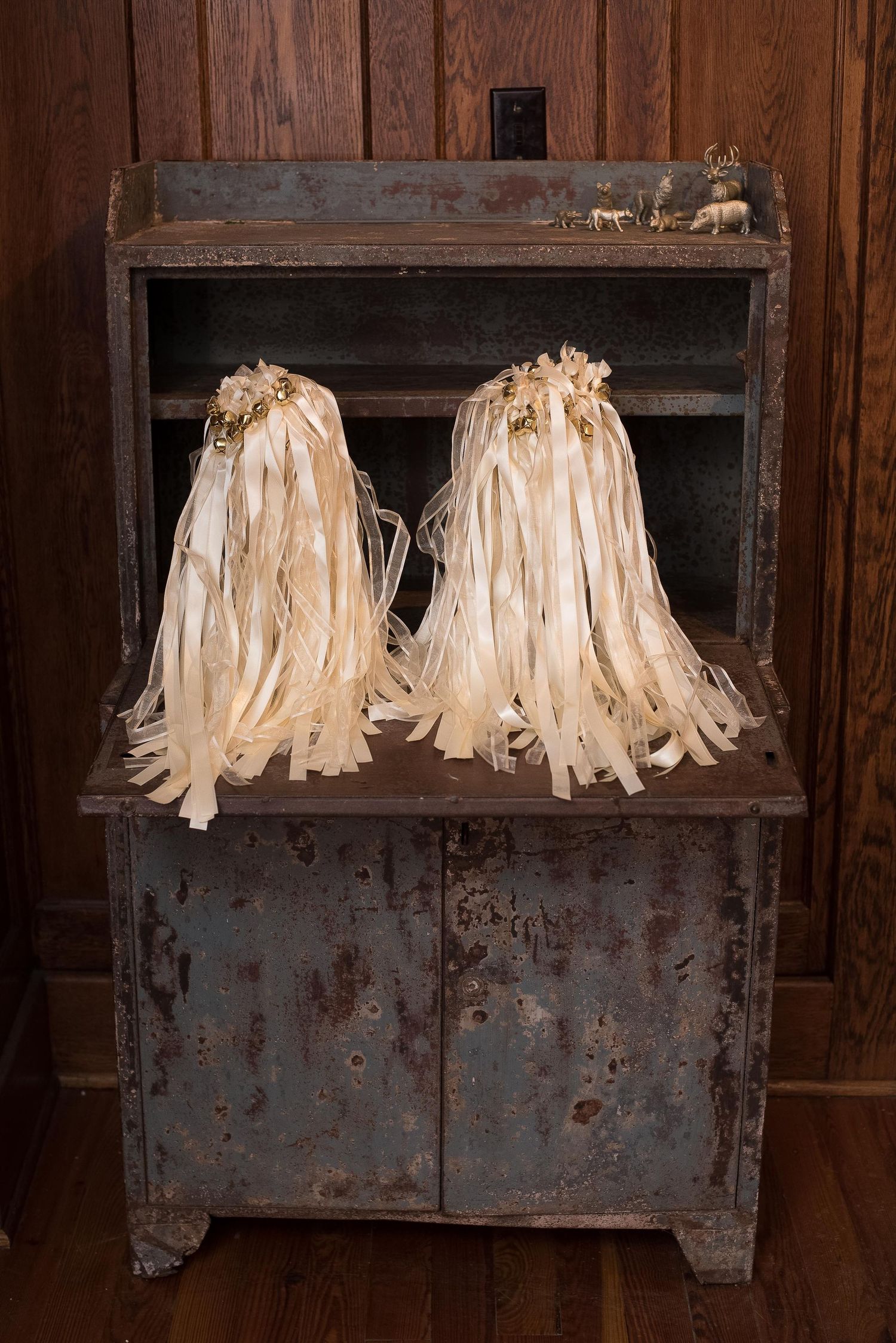 Two cream ribbon wand bouquets with gold accents displayed on a rustic vintage metal cabinet with wooden backdrop.