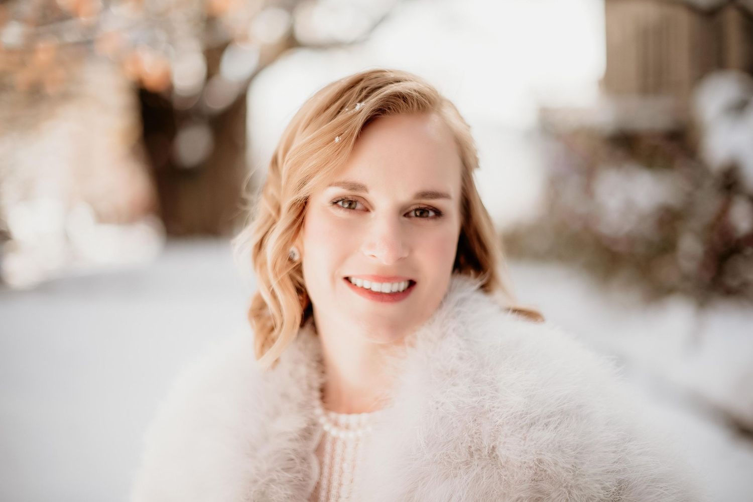Smiling blonde woman in white fuzzy sweater posing outdoors in a snowy winter setting.
