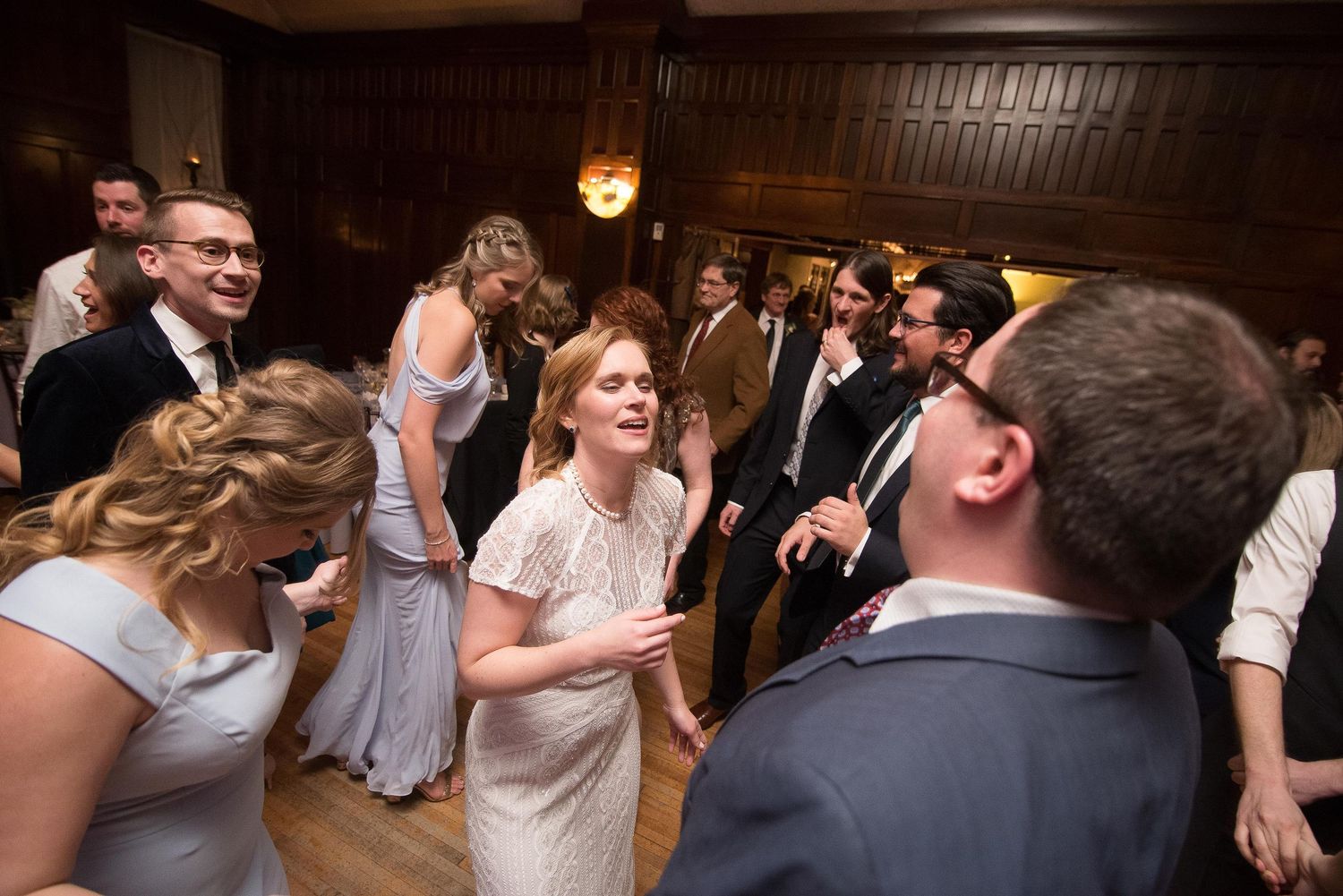Guests dancing and celebrating at an elegant wedding reception in a wood-paneled ballroom.