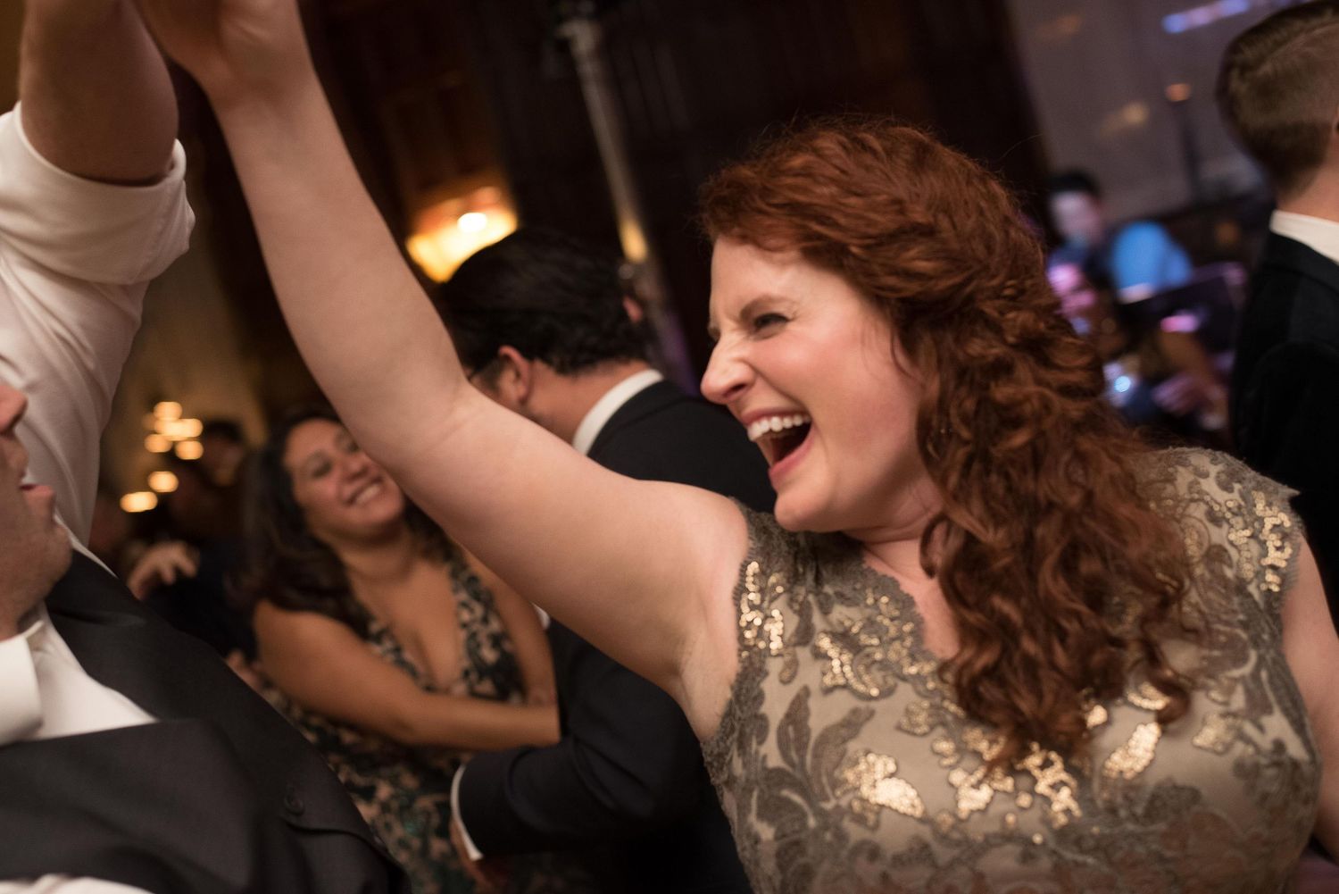 Joyful woman with curly red hair dancing and laughing at a formal evening celebration or wedding reception.