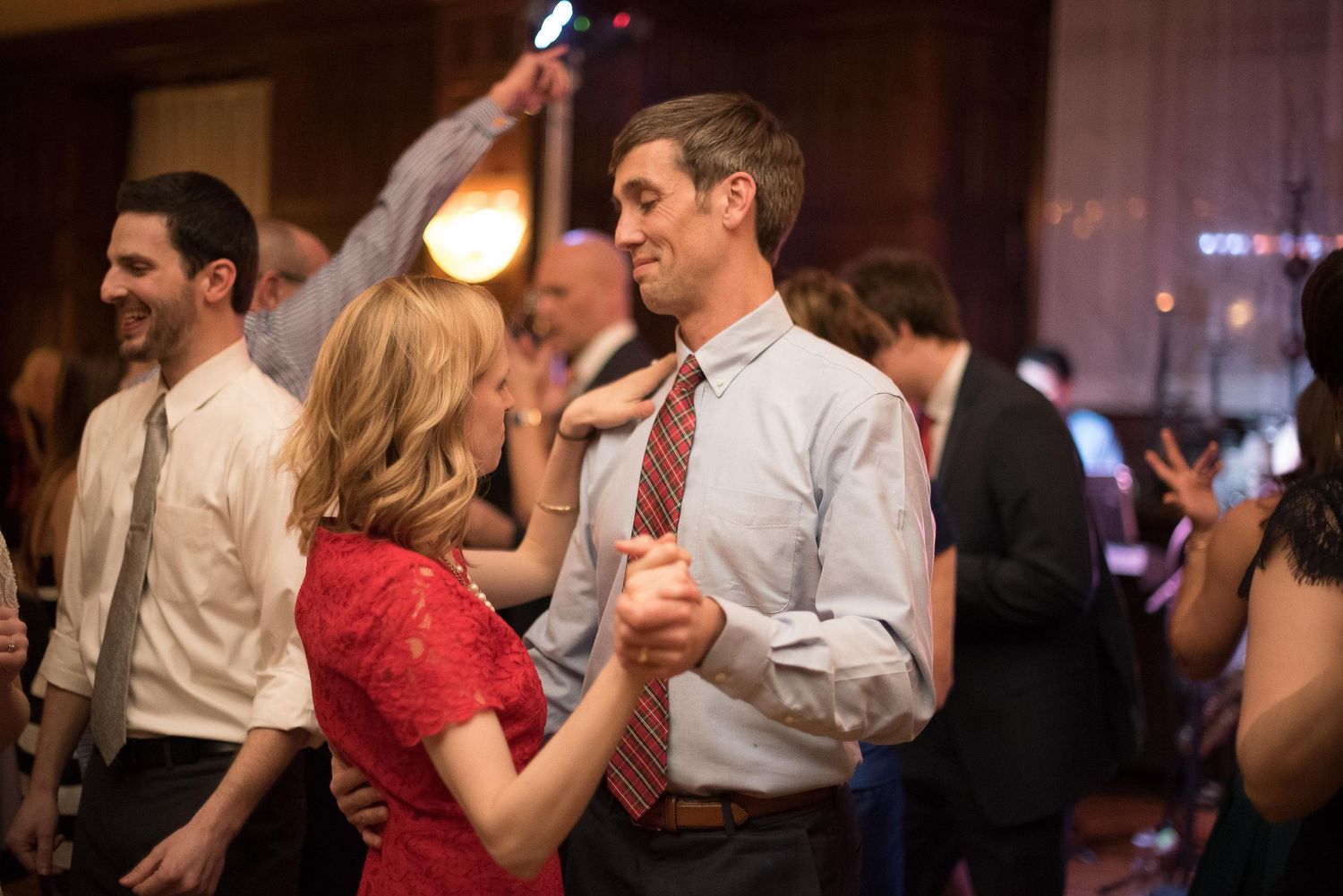Couple dancing together at a formal event, smiling, surrounded by other guests in elegant attire.