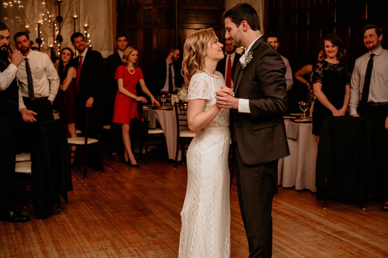Couple shares romantic first dance at wedding reception while guests watch in warmly lit elegant venue.