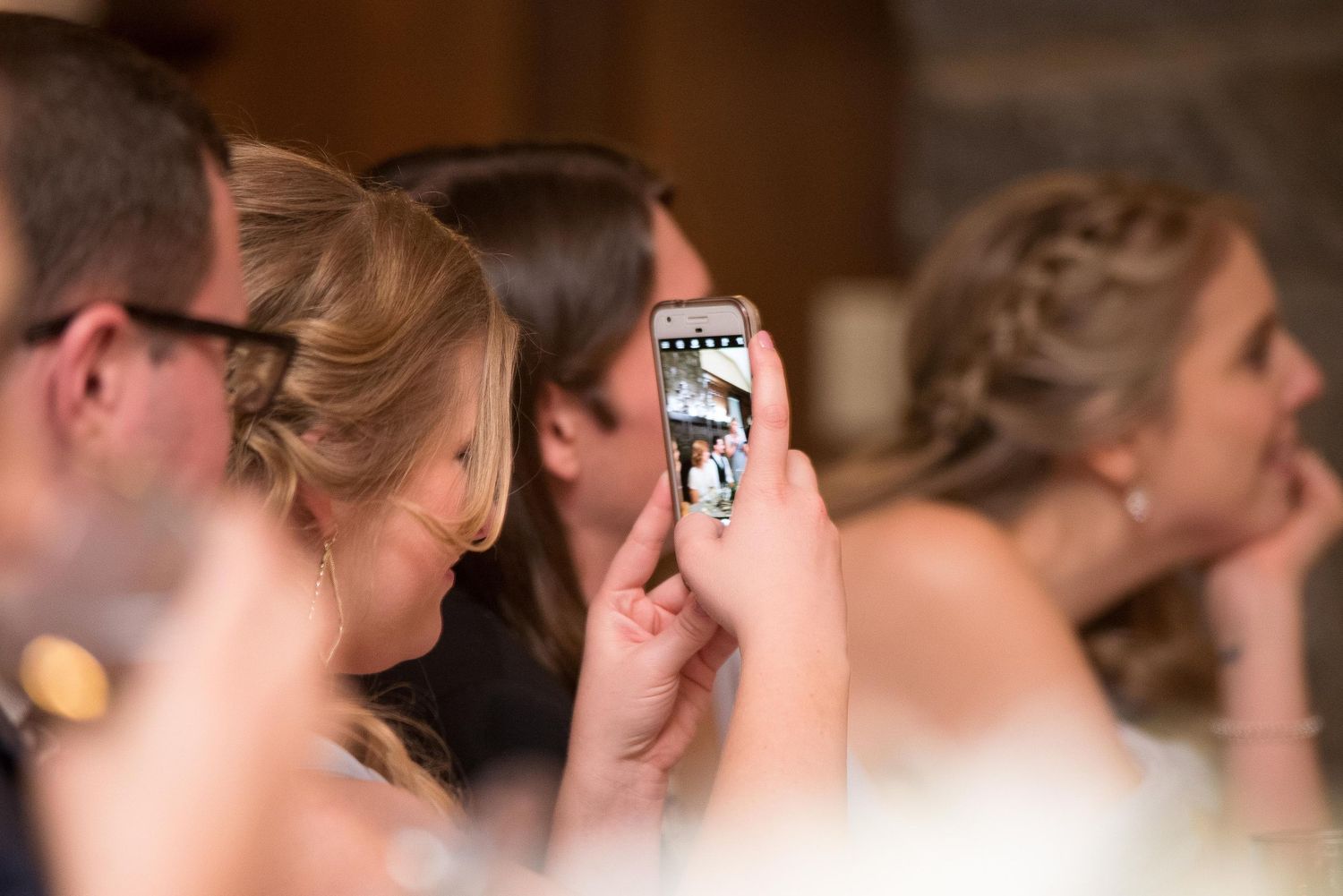 A wedding guest photographs the bride using a smartphone during the reception ceremony.