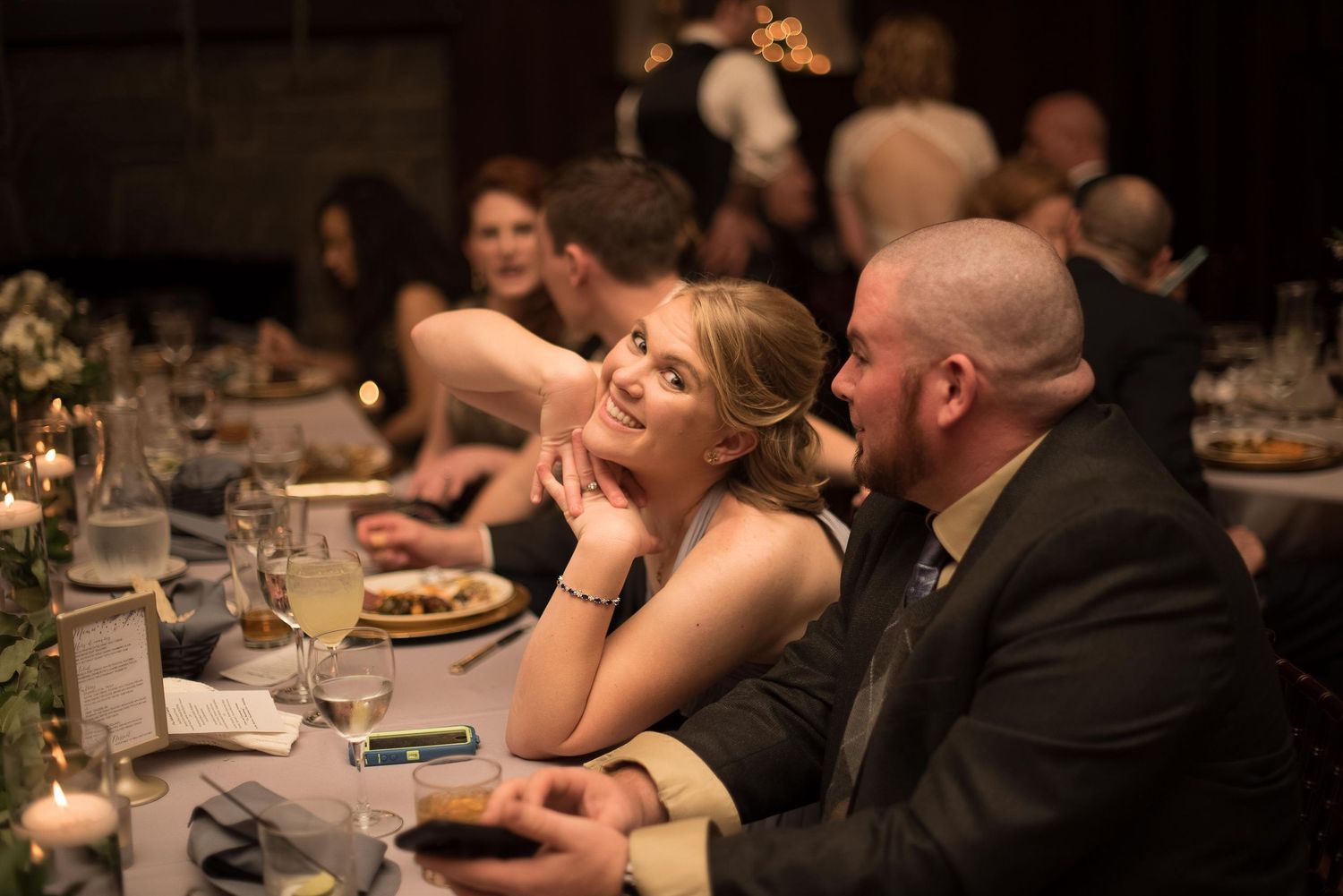 Elegant couple smiling at a formal dinner gala, surrounded by candlelit tables and guests in evening attire.