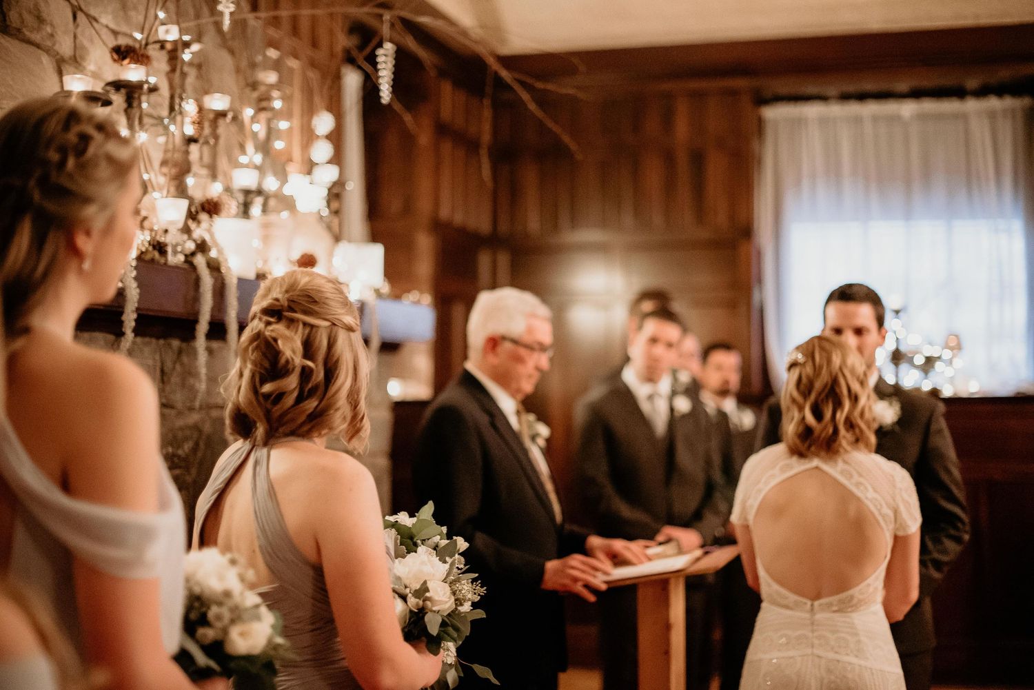 Wedding ceremony with bride, groom, and officiant at rustic indoor venue with elegant floral decor.