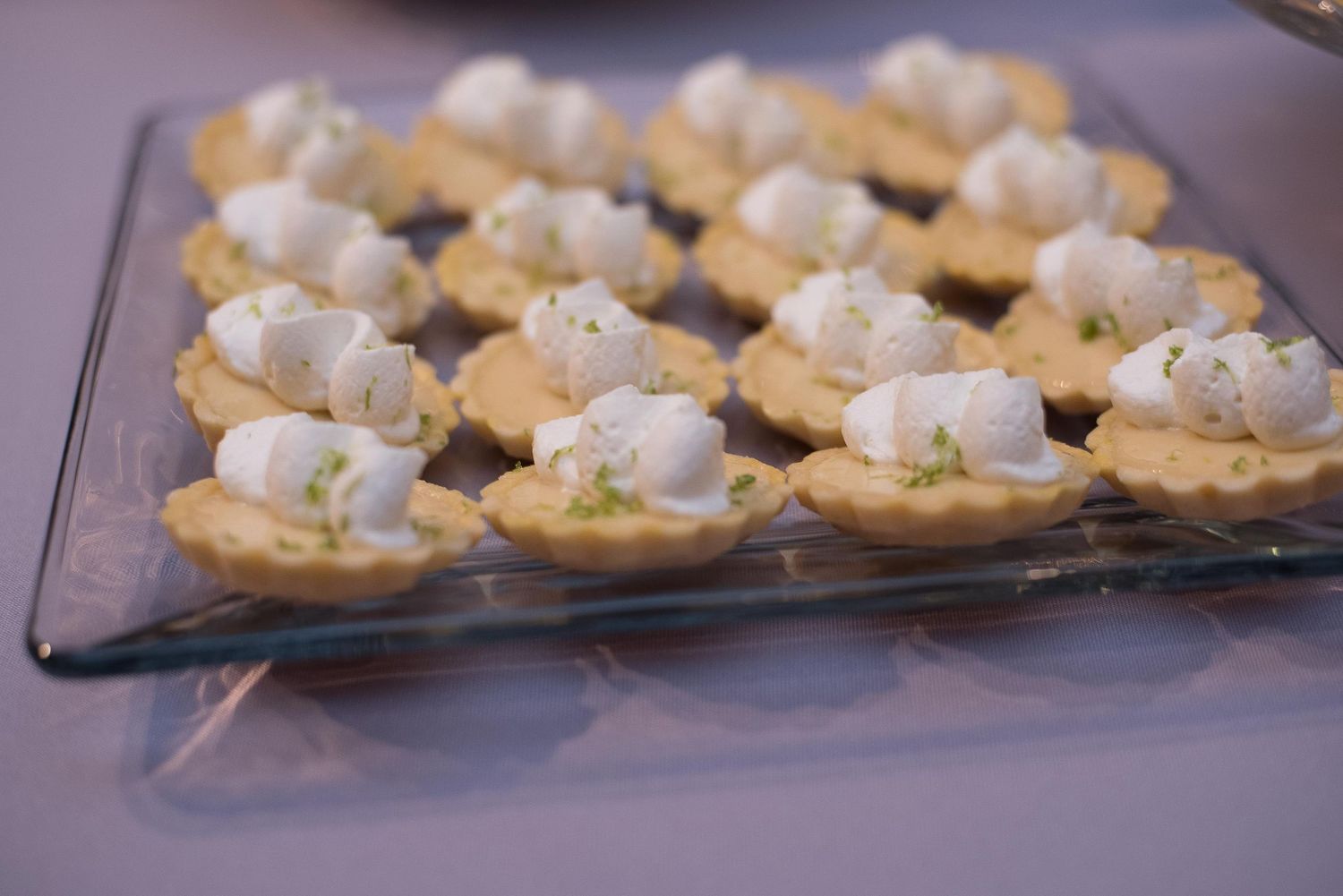 Mini tart shells filled with creamy topping and garnished with herbs arranged on a glass serving tray.