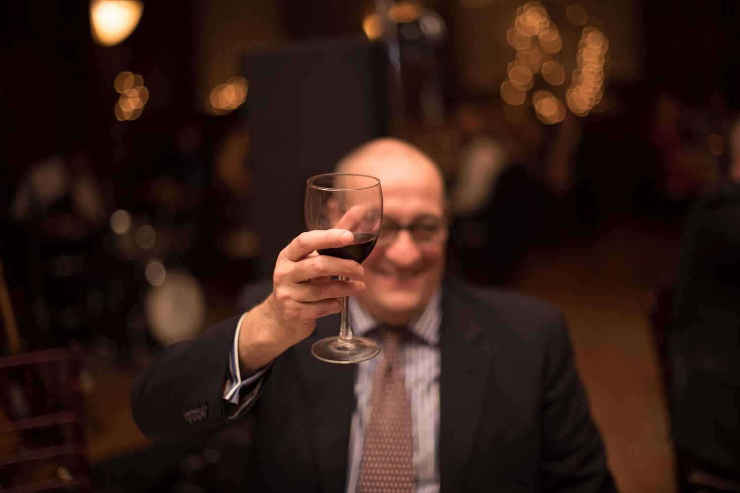 Man in suit raising a glass of red wine in a toast at an elegant evening event.