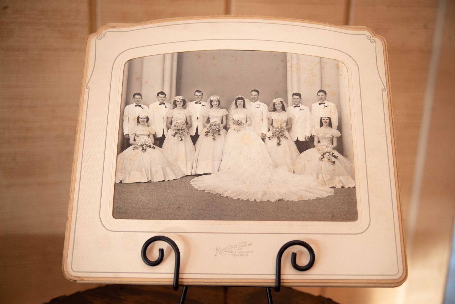 Vintage black and white wedding photo displayed on an easel, showing a bride, groom, and wedding party in formal attire.