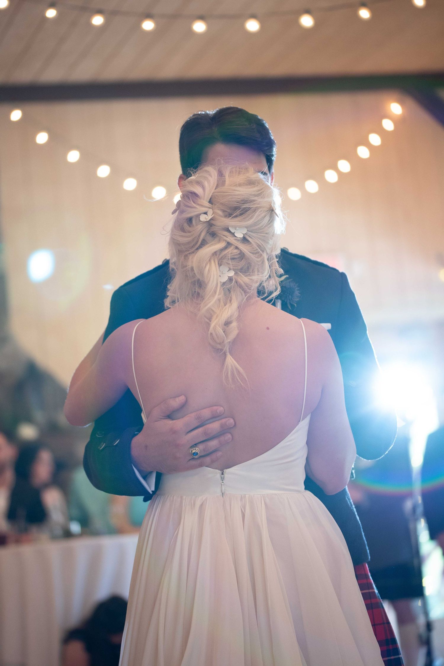 Bride and groom share their first dance, fairy lights glowing in background at wedding reception.