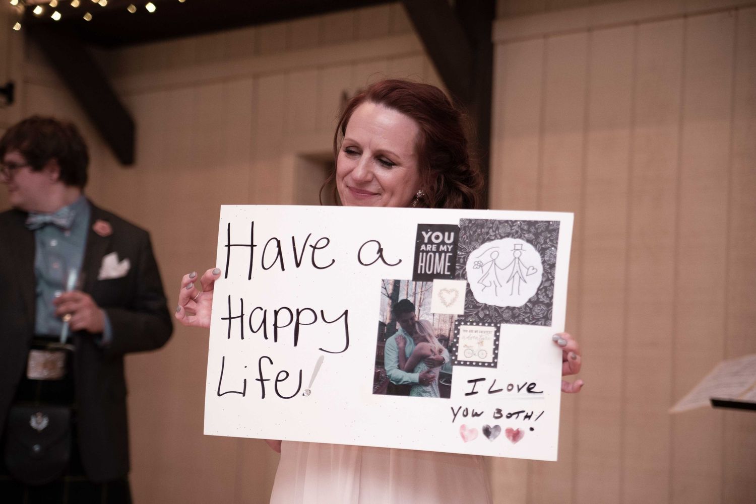 Woman holding a handmade wedding sign reading Have a Happy Life with photos and I Love You Both message.