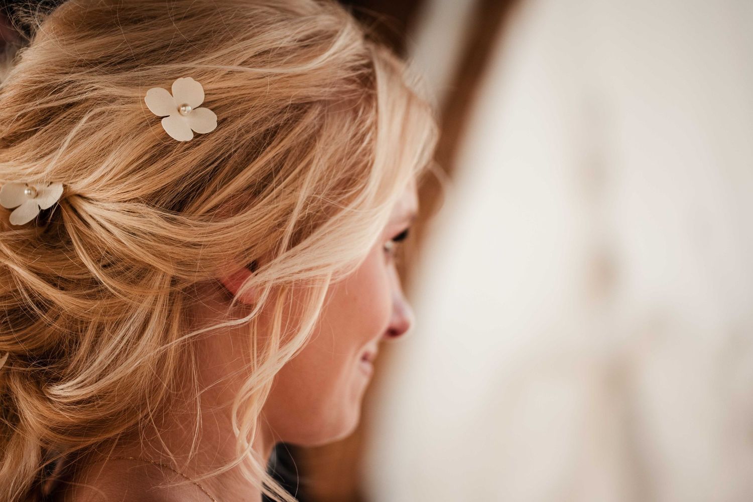 Close-up of a blonde bride with elegant half-up hairstyle adorned with delicate white flower hair pins.