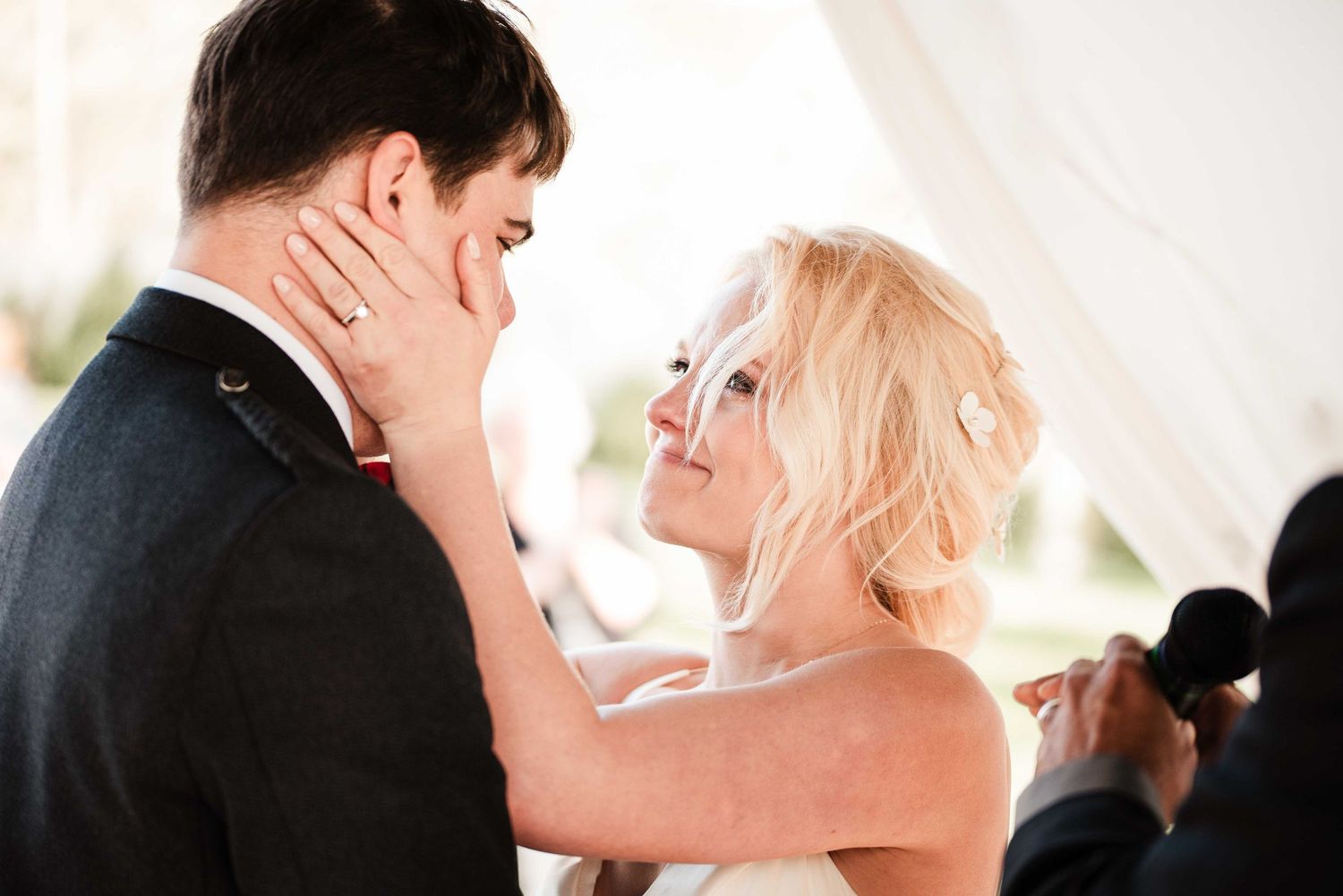 Radiant blonde bride tenderly holds grooms face during intimate first dance at elegant wedding celebration.