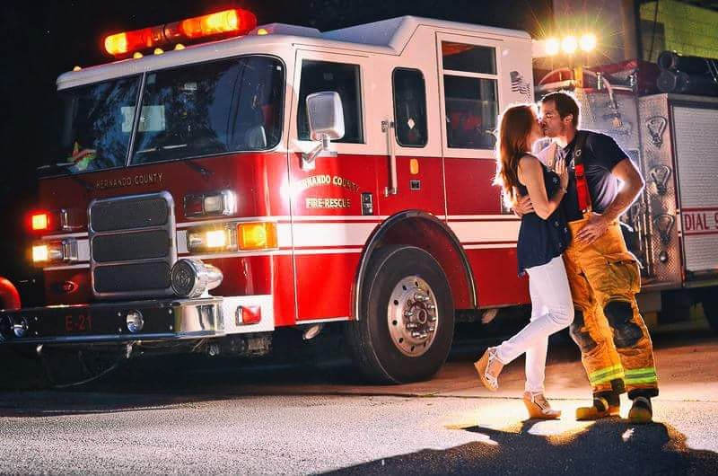 Couple sharing romantic kiss in front of red fire truck at night.