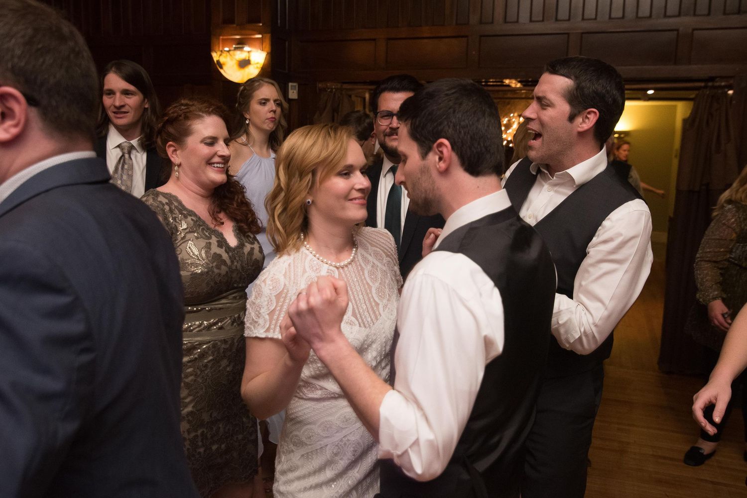 Couple shares a romantic dance at a wedding reception surrounded by smiling guests in elegant attire.