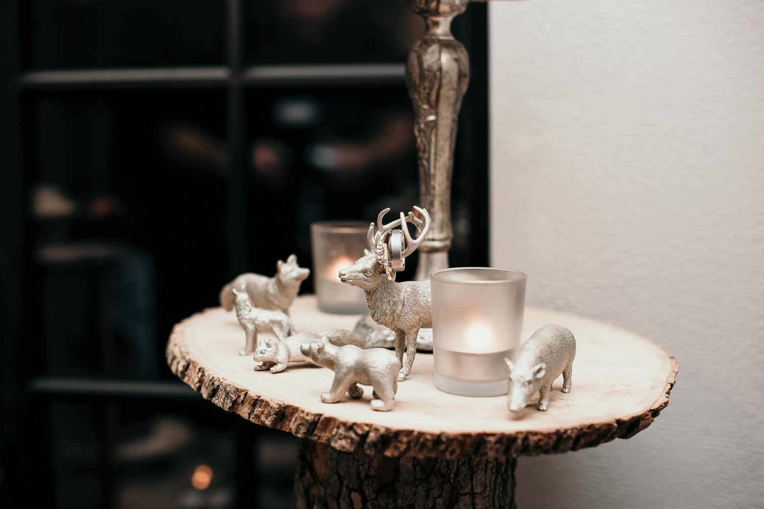 Silver animal figurines and frosted candle holders arranged on a rustic wood slice centerpiece.