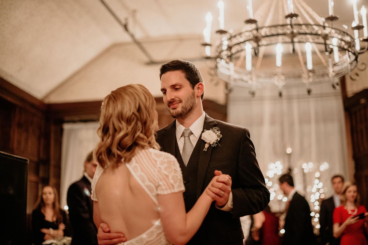 Bride and groom share their first dance under a chandelier in an elegant wedding reception venue.