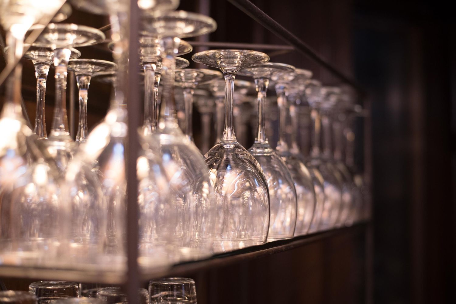 Rows of elegant crystal wine glasses stored upside down on a wooden bar shelf in a restaurant.