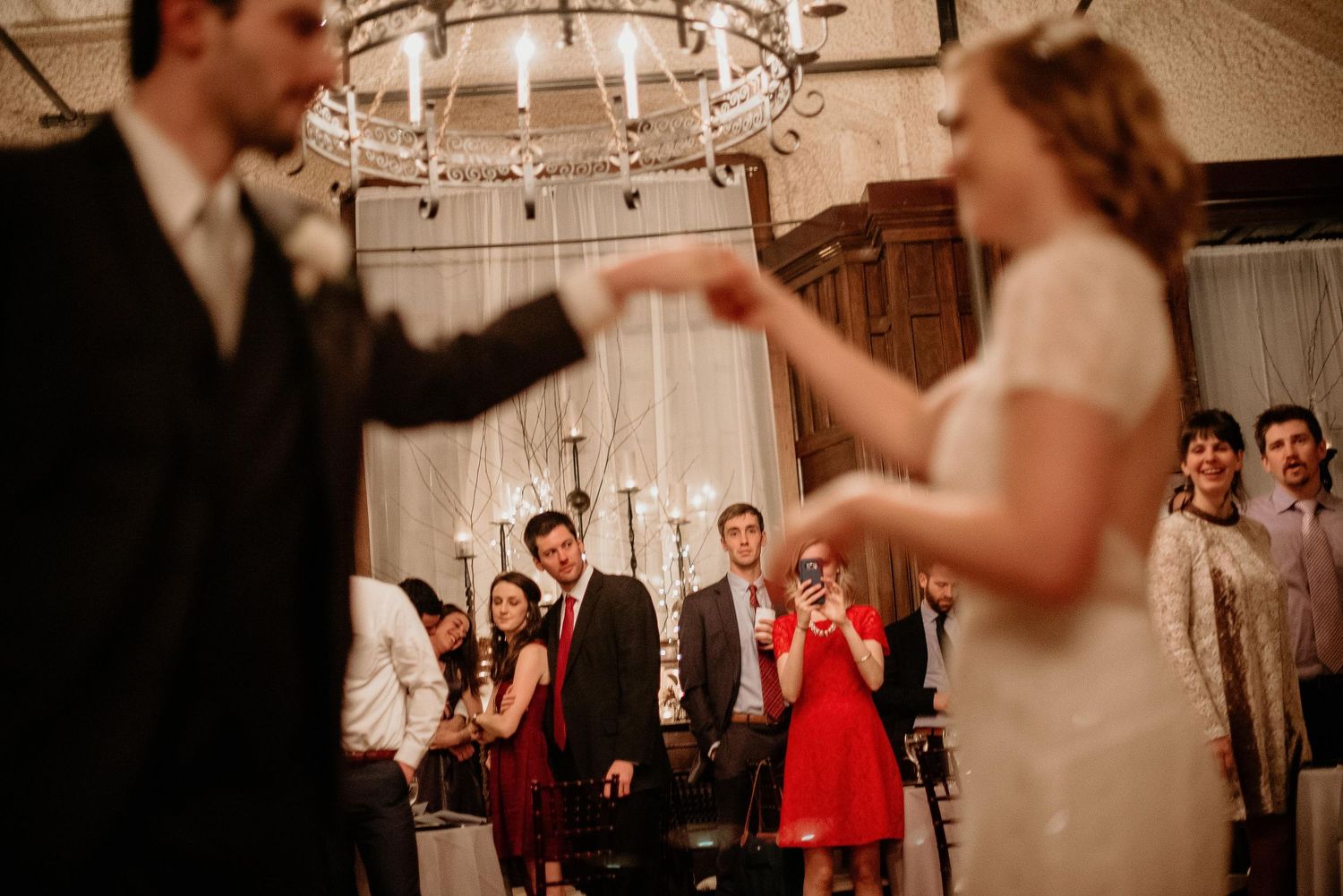 Bride and groom share first dance at elegant wedding reception with guests watching in candlelit ballroom.