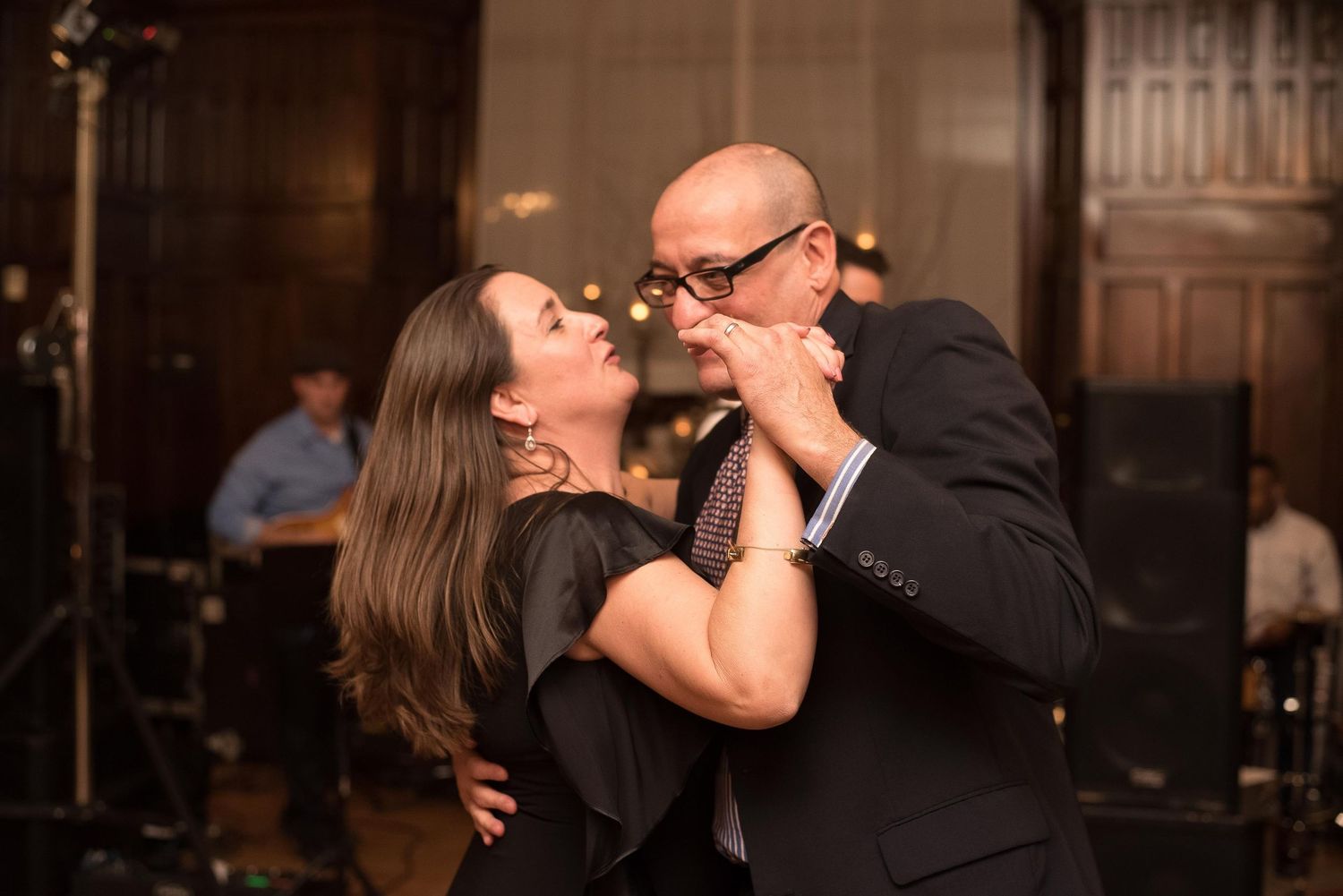 Couple dancing closely together at formal indoor event, man in suit and woman in black dress.
