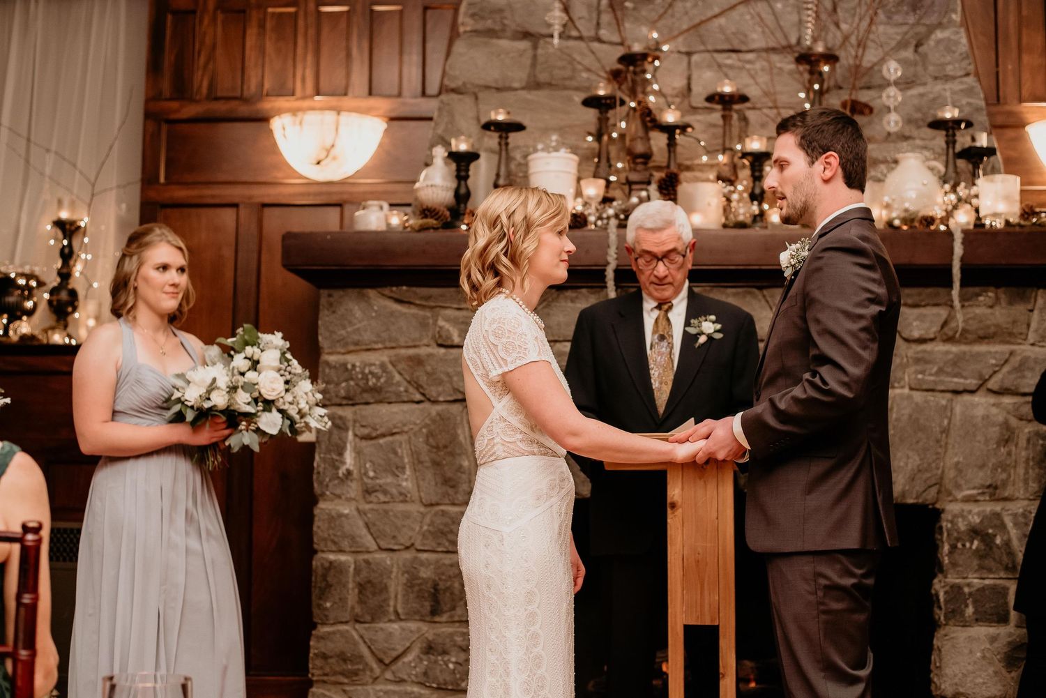 Bride and groom exchange vows at indoor wedding ceremony with stone fireplace and candles.