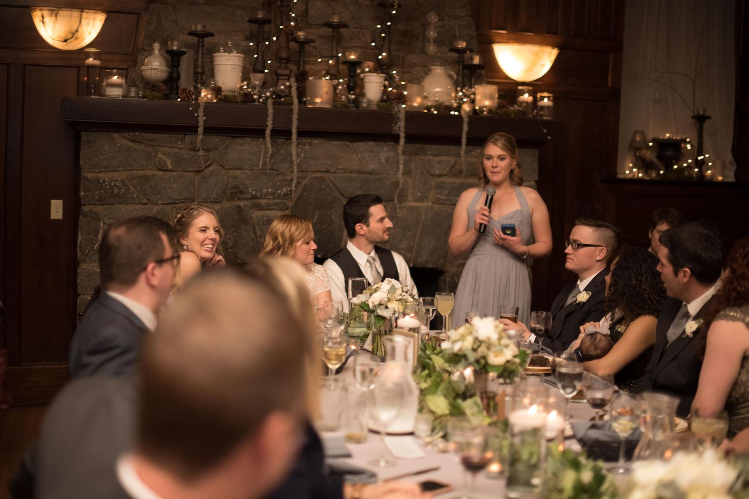 Woman giving a toast speech at an elegant wedding reception dinner with guests seated at a decorated table.
