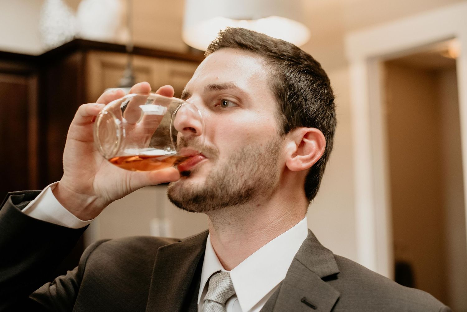 Man in suit drinking whiskey from a glass tumbler at a formal event.