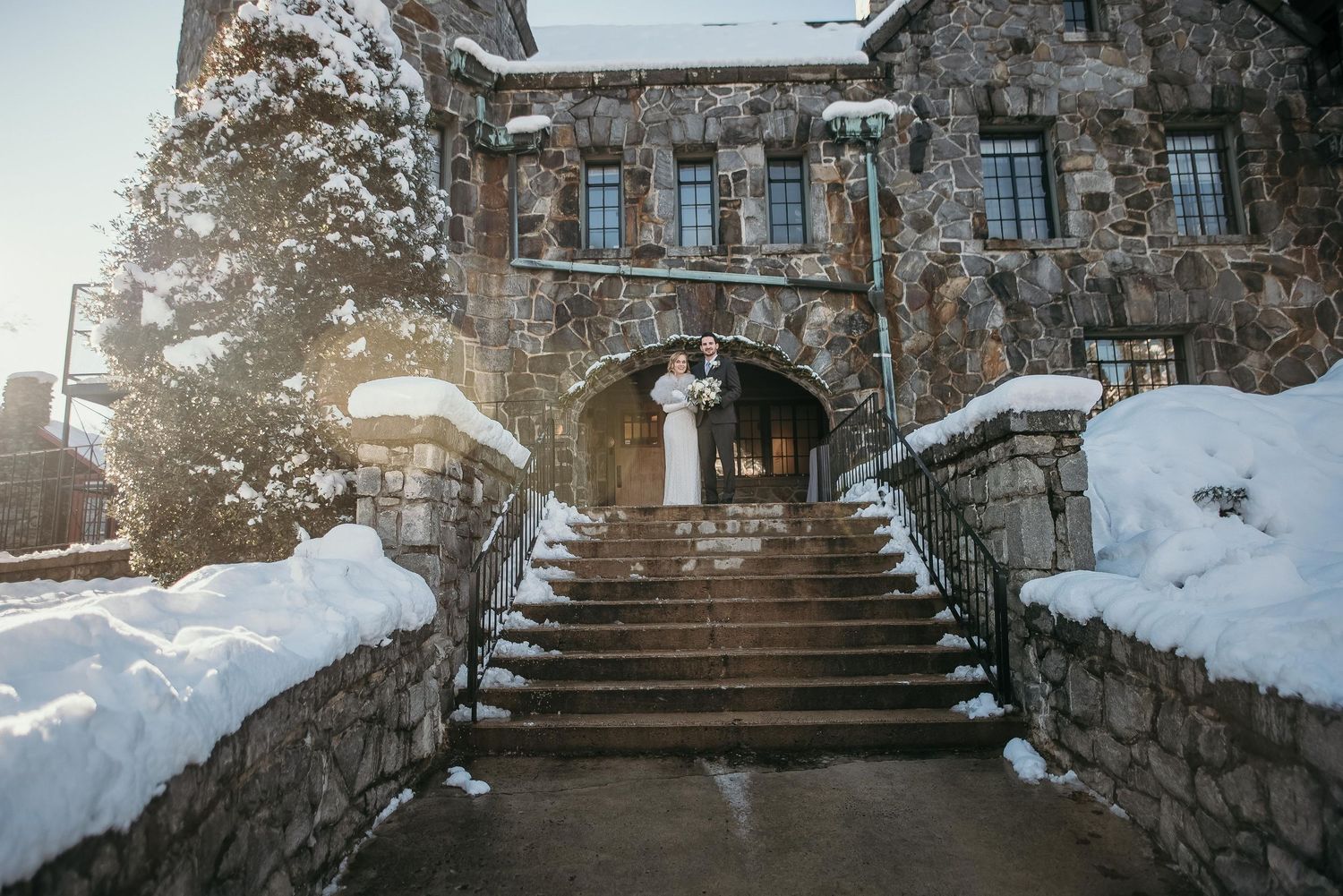 Bride and groom embrace on snowy stone castle steps in a stunning winter wedding scene.