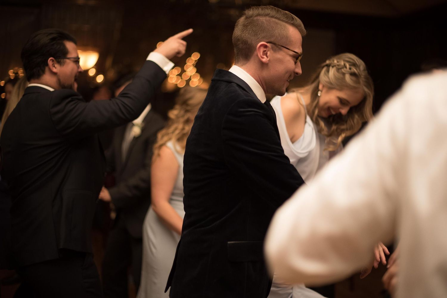 Couple dancing together at elegant wedding reception in dimly lit venue with guests celebrating around them.
