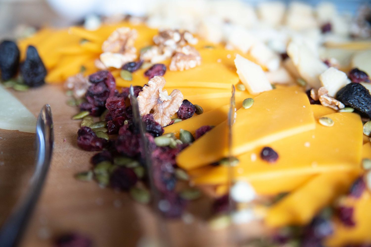 Close-up of a charcuterie board with sliced cheddar cheese, dried cranberries, walnuts, and mixed nuts.